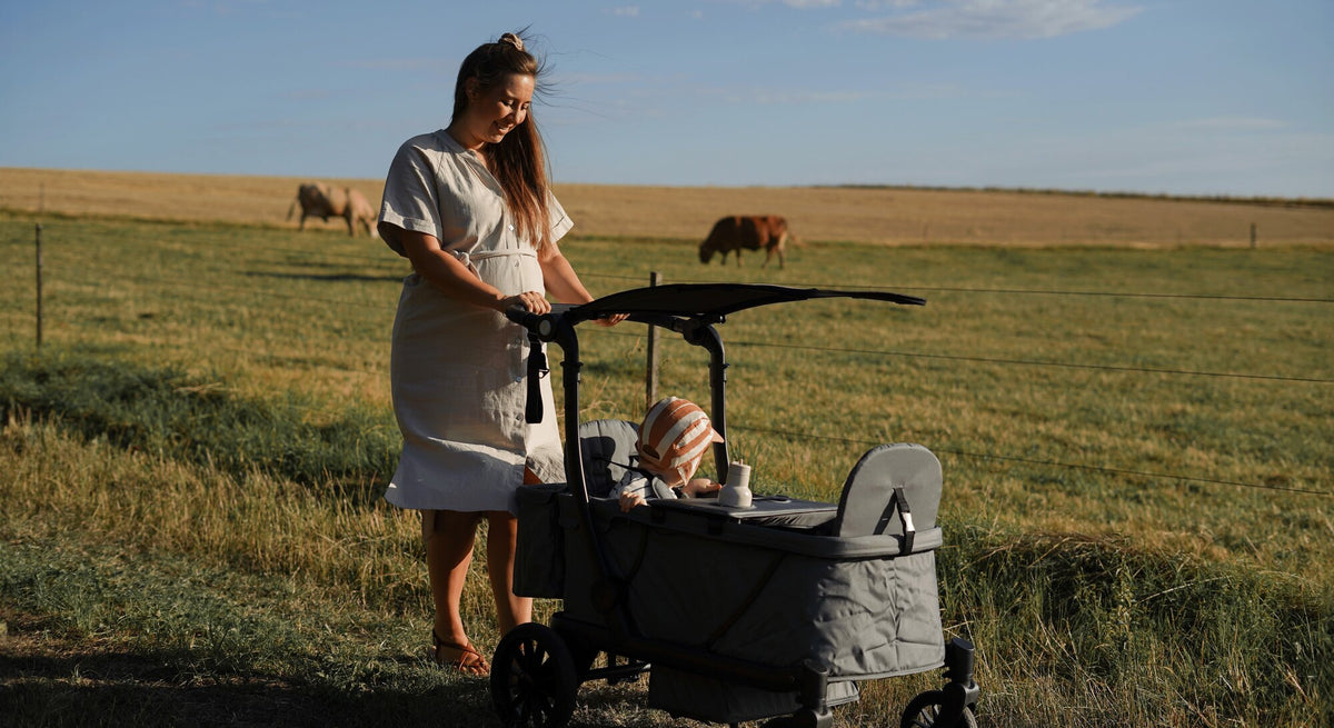 Mutter schiebt den KETTLER Bollerwagen mit Baby über eine Weide im Abendlicht