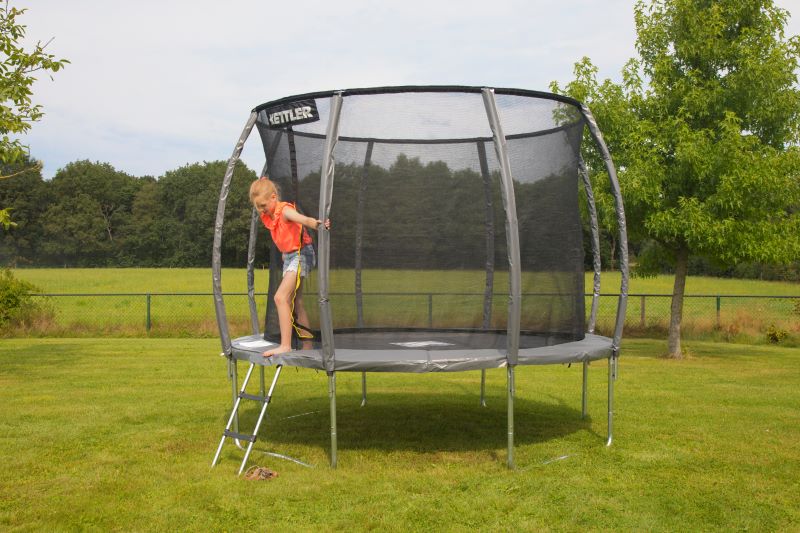 Ein Kind steigt über eine Leiter auf das KETTLER Trampolin JUMP 305 im Garten.