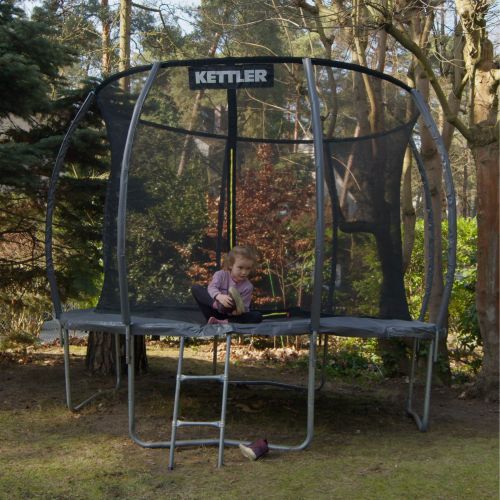 Ein Kind das KETTLER Trampolin JUMP 305 im Garten. Es sieht sehr idyllisch aus.