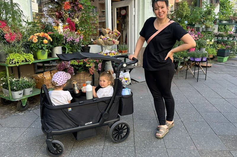 Mutter mit zwei Kindern im KETTLER Klappbollerwagen COMPACT vor einem Blumenladen